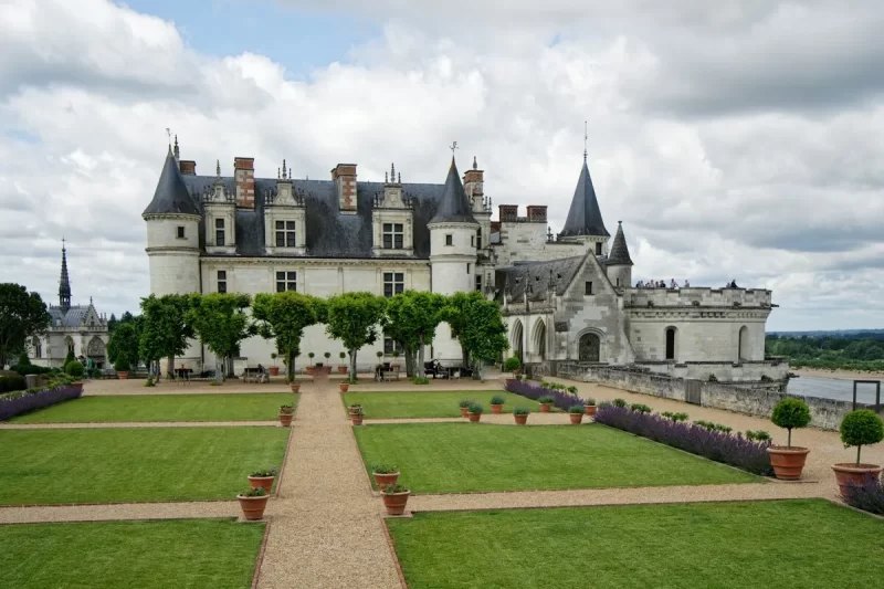 Castelo de Amboise na França, com jardins bem cuidados, árvores topiadas e vista para o rio.