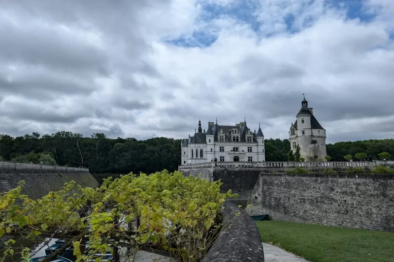 Château de Chenonceau na França, com torreões e arquitetura renascentista, visto através de muralhas e vegetação.