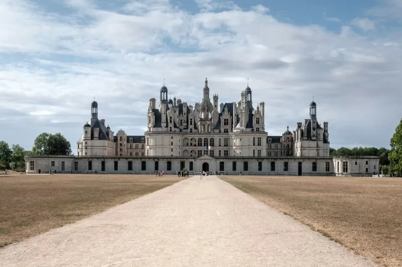 Castelo de Chambord na França, com arquitetura renascentista, torreões e cúpulas, visto de uma longa alameda.