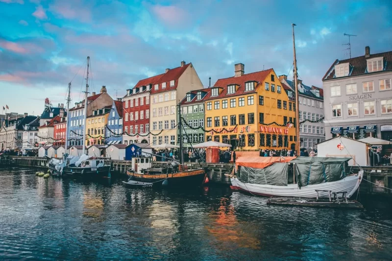 Canais de Nyhavn em Copenhague com barcos, edifícios coloridos e decoração festiva.