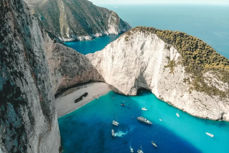 Vista aérea da deslumbrante Navagio Beach (Praia do Naufrágio) em Zakynthos, Grécia, com suas falésias brancas imponentes, mar azul-turquesa intenso e um navio naufragado na areia branca.
