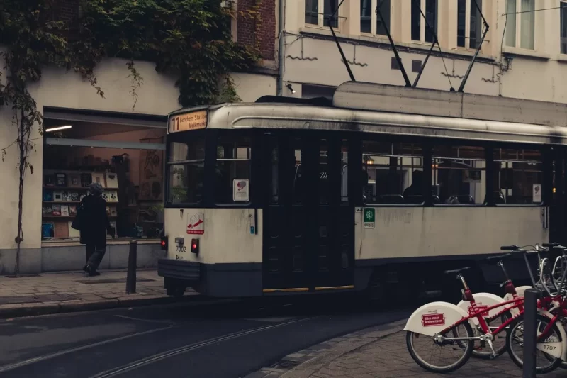Bonde clássico branco e preto circulando em uma rua de Antuérpia, Bélgica, com edifícios históricos e uma estação de bicicletas ao lado, mostrando o transporte público em Antuérpia.