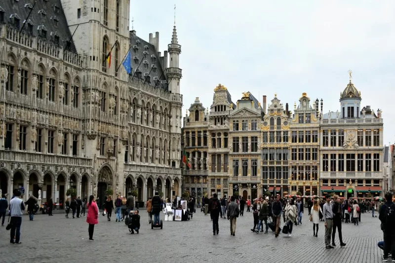 Praça histórica movimentada na Bélgica, com edifícios ornamentados de estilo gótico e barroco, representando a riqueza arquitetônica que pode ser encontrada em cidades como Antuérpia.