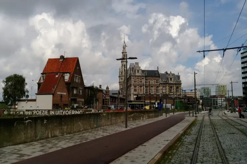Paisagem urbana de Antuérpia, Bélgica, com edifícios históricos, trilhos de bonde, e um céu nublado, mostrando a arquitetura e a atmosfera de Antuérpia.