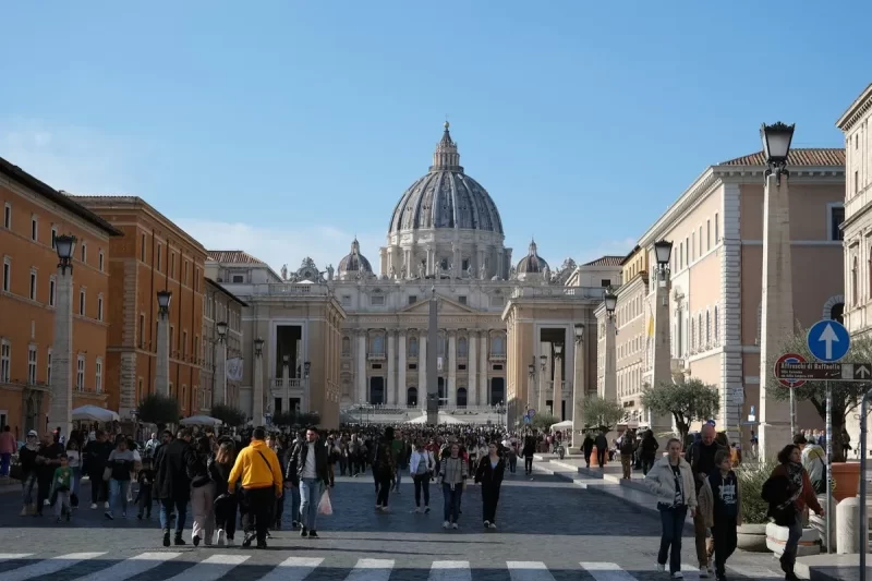 Vista externa da Basílica de São Pedro no Vaticano, com uma multidão de pessoas caminhando em direção a ela, um destino que abriga a famosa Capela Sistina.