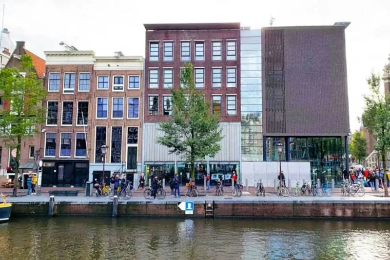 A fachada externa da Casa de Anne Frank em Amsterdã, um complexo de edifícios históricos e modernos à beira de um canal, com a palavra-chave "Casa de Anne Frank".