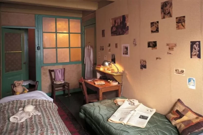 O quarto de Anne Frank na Casa de Anne Frank, com camas, escrivaninha e as paredes decoradas com imagens que ela colecionava, oferecendo um vislumbre pessoal de sua vida no esconderijo.
