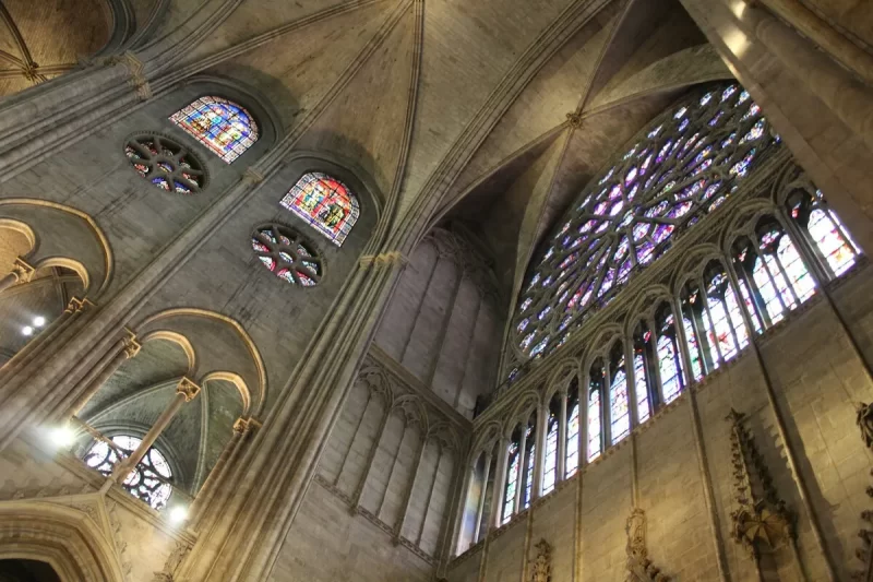  Vista interna da Catedral de Notre-Dame, com seus grandes vitrais coloridos, rosetas intrincadas e o teto abobadado de pedra, destacando a arte gótica e a iluminação.