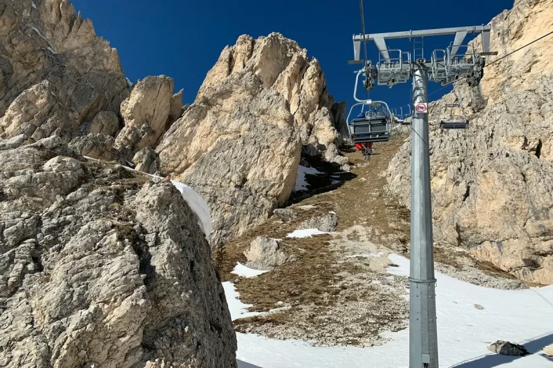 Bondinho subindo entre picos rochosos imponentes nas Dolomitas, com neve e terreno árido