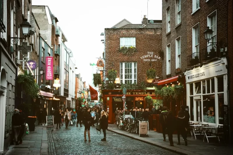Rua de paralelepípedos movimentada no bairro Temple Bar, Dublin, Irlanda, com o famoso pub The Temple Bar e pessoas passeando, capturando a atmosfera vibrante de Dublin na Irlanda.