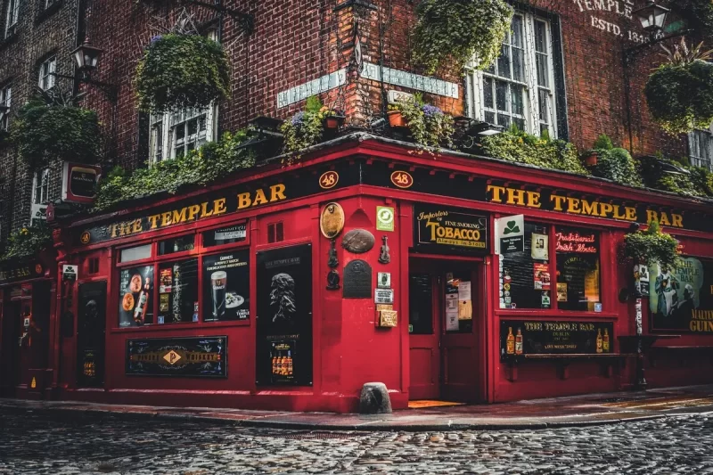 Fachada vermelha vibrante do famoso pub The Temple Bar na esquina de uma rua de paralelepípedos em Dublin, Irlanda, um marco essencial para quem visita Dublin na Irlanda.