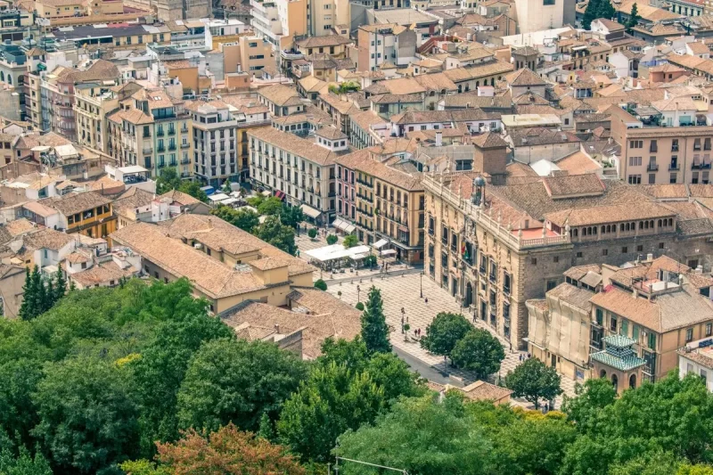 Vista aérea panorâmica do centro histórico de Granada, Espanha, com edifícios tradicionais de telhados de terracota, praças e áreas verdes, destacando a beleza de Granada.