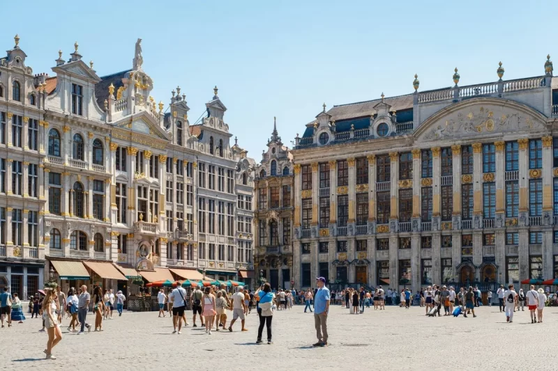 Grand Place em Bruxelas, Bélgica, edifícios históricos com fachadas douradas, turistas caminhando na praça.