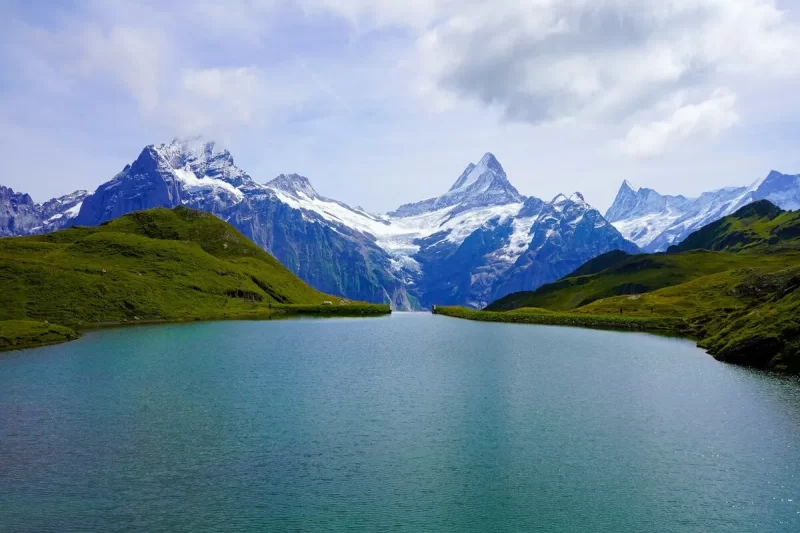 Vista serena do Lago Bachalpsee com águas claras e as imponentes montanhas nevadas dos Alpes Suíços ao fundo, representando a beleza natural da região de Interlaken.