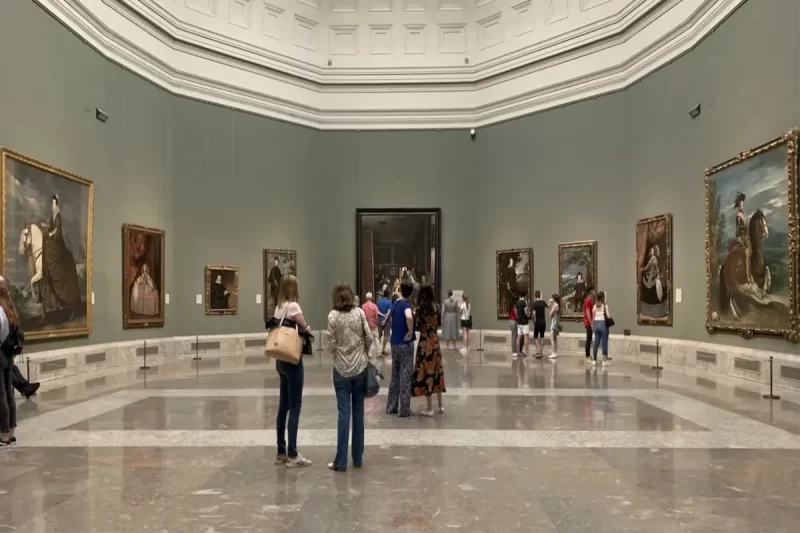 Interior espaçoso do Museu do Prado em Madri, com visitantes admirando uma vasta coleção de obras de arte clássicas expostas nas paredes e ao longo do salão.