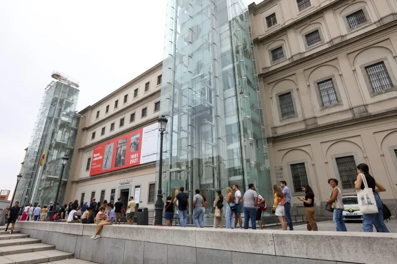 Entrada do Museu Reina Sofia em Madrid com torres de elevador de vidro, fachada clássica e visitantes em fila