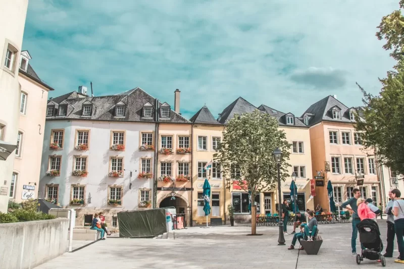Rua charmosa na capital de Luxemburgo, o país mais rico da Europa, com prédios coloridos, cafés e pessoas aproveitando o dia.