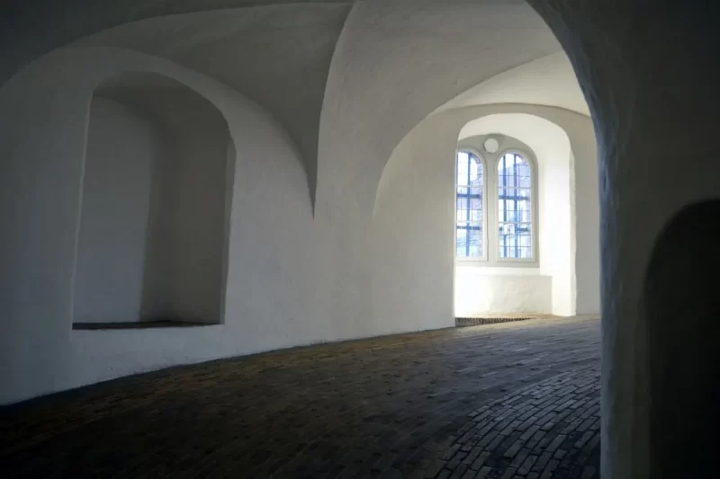 O interior de um castelo em Copenhague, mostrando um corredor abobadado de tijolos e uma janela com iluminação natural. A imagem destaca a arquitetura histórica da cidade.