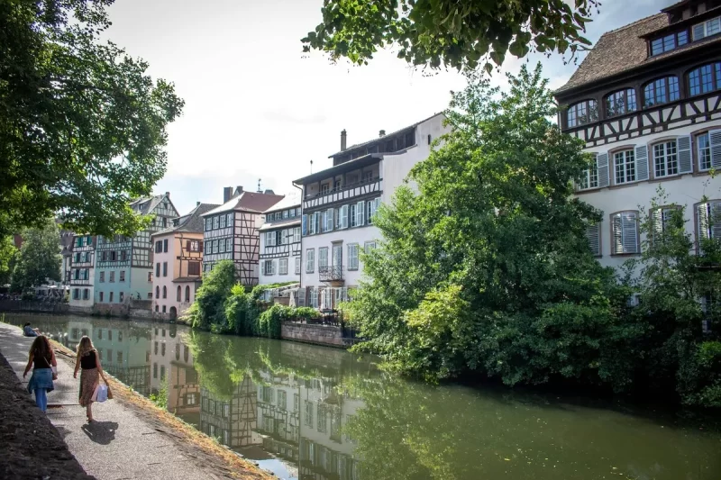 Vista de Estrasburgo com o rio, casas enxaimel e pessoas caminhando.