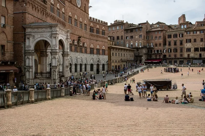 Turistas e moradores relaxam na Piazza del Campo, em Siena, uma das mais belas cidades na Toscana. A fotografia mostra o icónico Palazzo Pubblico com a sua arquitetura de tijolos.