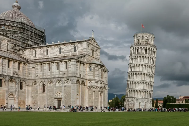 A icónica Torre de Pisa e a Catedral de Santa Maria Assunta no Campo dos Milagres, em Pisa, uma das mais famosas cidades na Toscana. A imagem mostra os monumentos de mármore branco em um dia nublado.