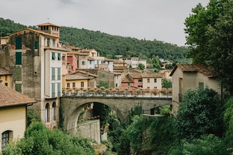 Uma vista pitoresca da vila de Loro Ciuffenna, uma das vilas medievais mais charmosas entre as cidades na Toscana. A imagem destaca a antiga ponte de pedra e as casas coloridas aninhadas na paisagem montanhosa.