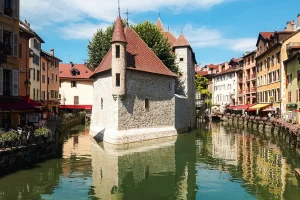 Palais de l’Isle em Annecy cercado por canais de água verde, com casas coloridas e cafés típicos franceses ao redor.