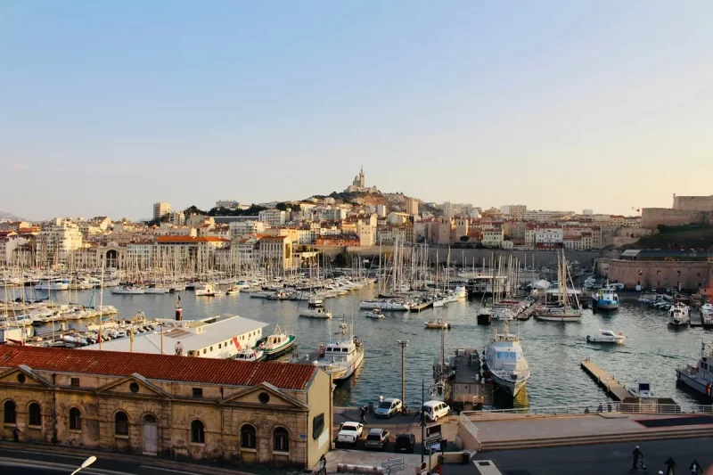 Vista panorâmica do Vieux-Port de Marselha com barcos atracados, prédios históricos e a Basílica de Notre-Dame de la Garde ao fundo.