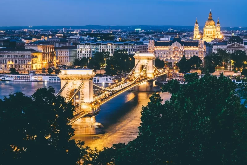 Ponte Széchenyi Lánchíd iluminada à noite em Budapeste, com o Rio Danúbio e edifícios históricos ao fundo.